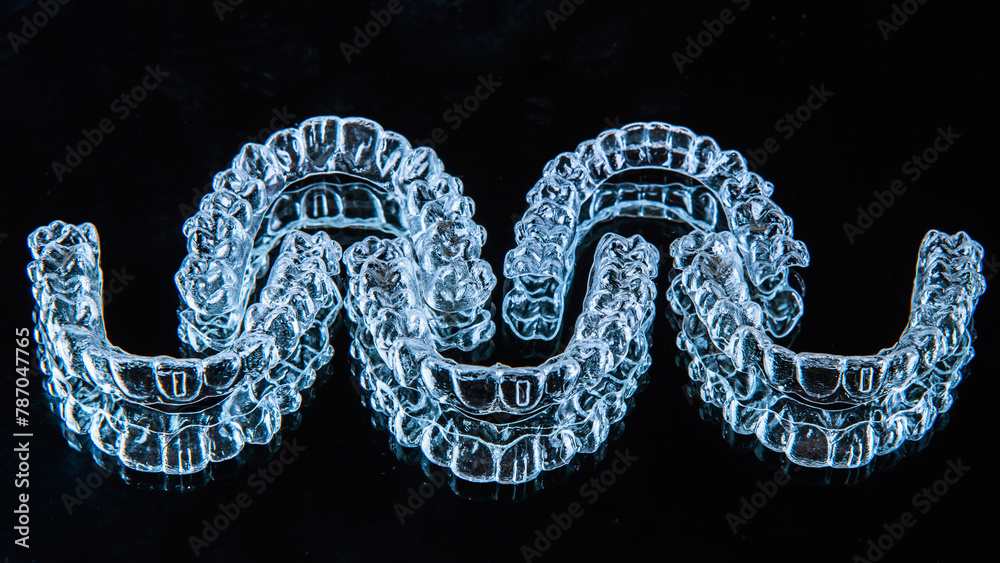 Obraz premium Invisible dental teeth brackets tooth aligners on black background. Plastic braces dentistry retainers to straighten teeth.