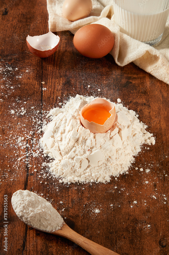 Preparation for healthy meal with a fresh egg cracked into flour for dough, decorated by a linen towel and a glass of milk. Wooden background, top view Preparation for healthy meal with a fresh egg cracked into flour for dough, decorated by a linen towel and a glass of milk. Wooden background, top view
