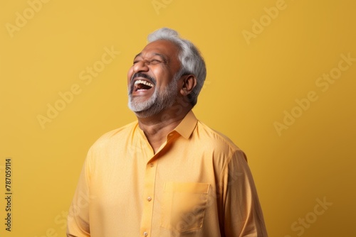 Portrait of a joyful indian man in his 60s sporting a long-sleeved thermal undershirt on pastel yellow background