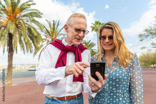 Happy senior couple portrait at seaside in Barcelona using mobile phone