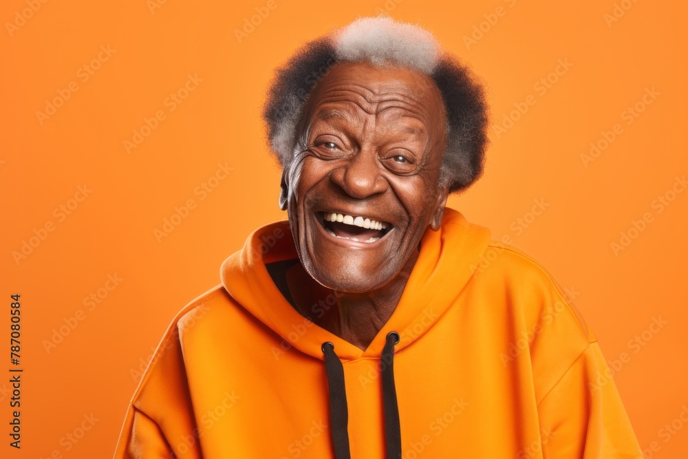 Portrait of a grinning afro-american man in his 80s wearing a thermal fleece pullover in front of soft orange background Portrait of a grinning afro-american man in his 80s wearing a thermal fleece pullover in front of soft orange background