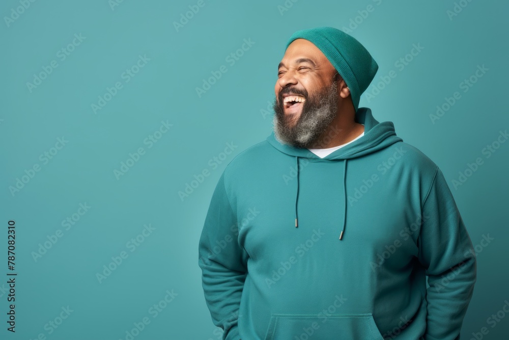 Portrait of a merry indian man in his 50s dressed in a comfy fleece pullover while standing against soft teal background Portrait of a merry indian man in his 50s dressed in a comfy fleece pullover while standing against soft teal background