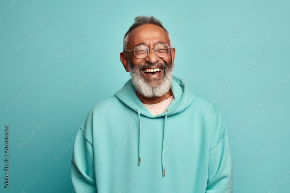 Portrait of a smiling indian man in his 80s sporting a comfortable hoodie over soft teal background Portrait of a smiling indian man in his 80s sporting a comfortable hoodie over soft teal background