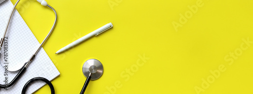 Stethoscope, notepad and pen on a yellow background, top view. Cardiology and healthcare concept. Auscultation device. Medical care concept. Medical instrument. Auscultation apparatus photo