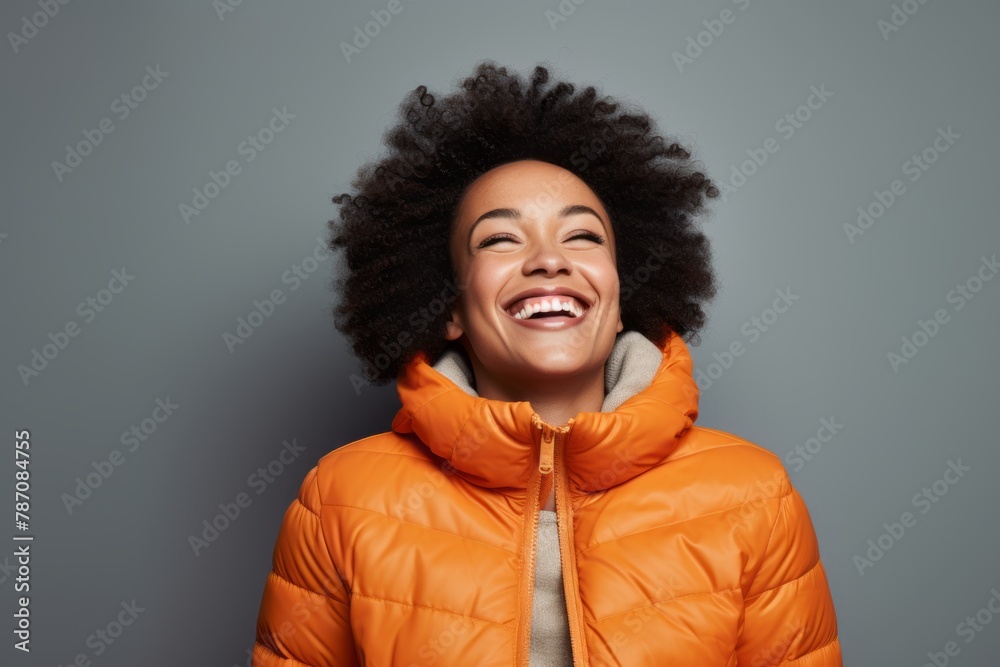 Portrait of a joyful afro-american woman in her 20s sporting a quilted insulated jacket in front of soft gray background Portrait of a joyful afro-american woman in her 20s sporting a quilted insulated jacket in front of soft gray background