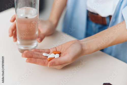 Woman taking pills with a glass of water at a table in front of her in a healthcare and medication concept photo
