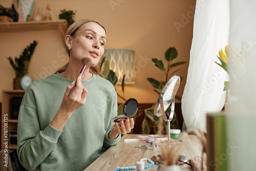 Portrait of elegant young woman doing make up looking in mirror by window copy space