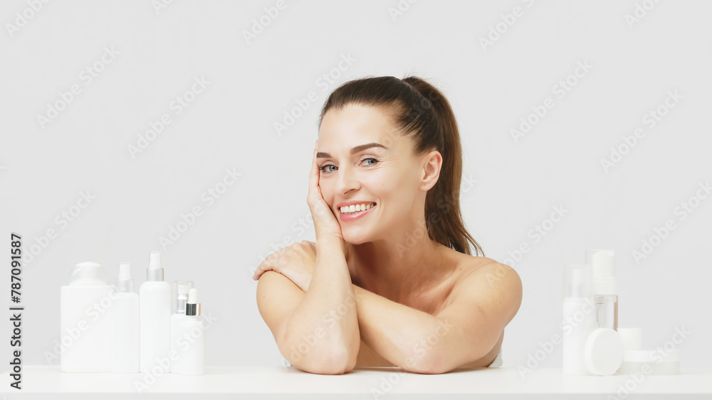 Portrait of a happy attractive middle-aged woman next to mock-ups of jars with cream and cosmetology natural cosmetics. Advertising of spa treatments, anti-aging care products for delicate dry skin. Portrait of a happy attractive middle-aged woman next to mock-ups of jars with cream and cosmetology natural cosmetics. Advertising of spa treatments, anti-aging care products for delicate dry skin.