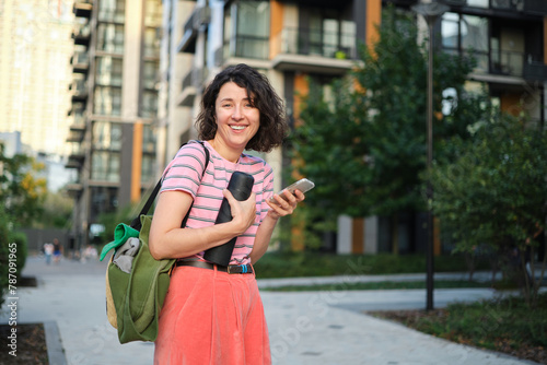Summer sunny lifestyle portrait of stylish hipster woman walking on the street, wearing cute trendy outfit, smiling enjoy her weekends, travel with bag. High quality photo