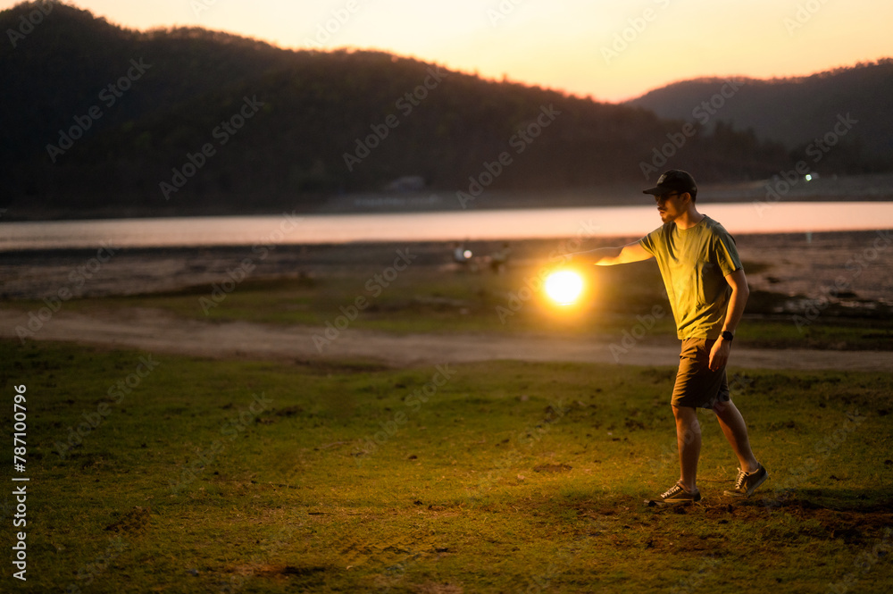 Casual man in a chair holding a lit lantern by a peaceful lake during twilight, creating a relaxing mood.