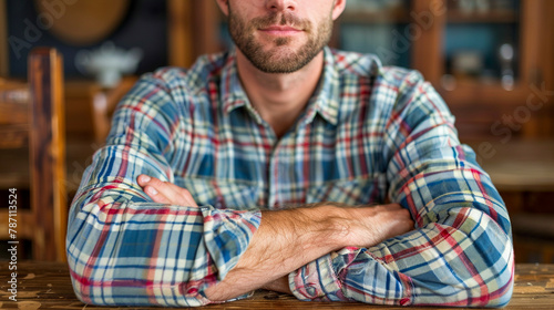 A man in a plaid shirt is sitting at a table with his arms crossed. photo