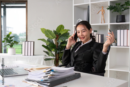 Asian female accountant Discussing business over the phone in an office with work plan documents on the table
