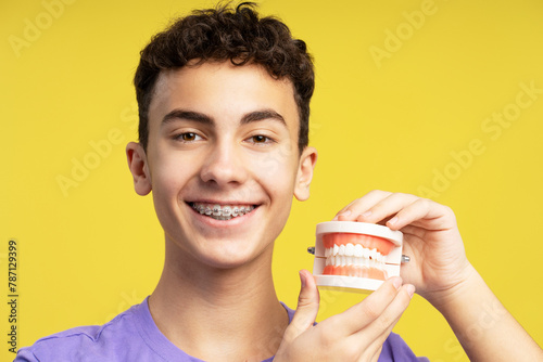 Attractive smiling boy, teenager with braces holding jaw, looking at camera