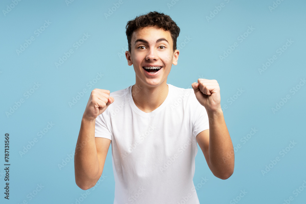 Fototapeta premium Happy excited fan boy with braces cheering, hands up, open mouth looking at camera