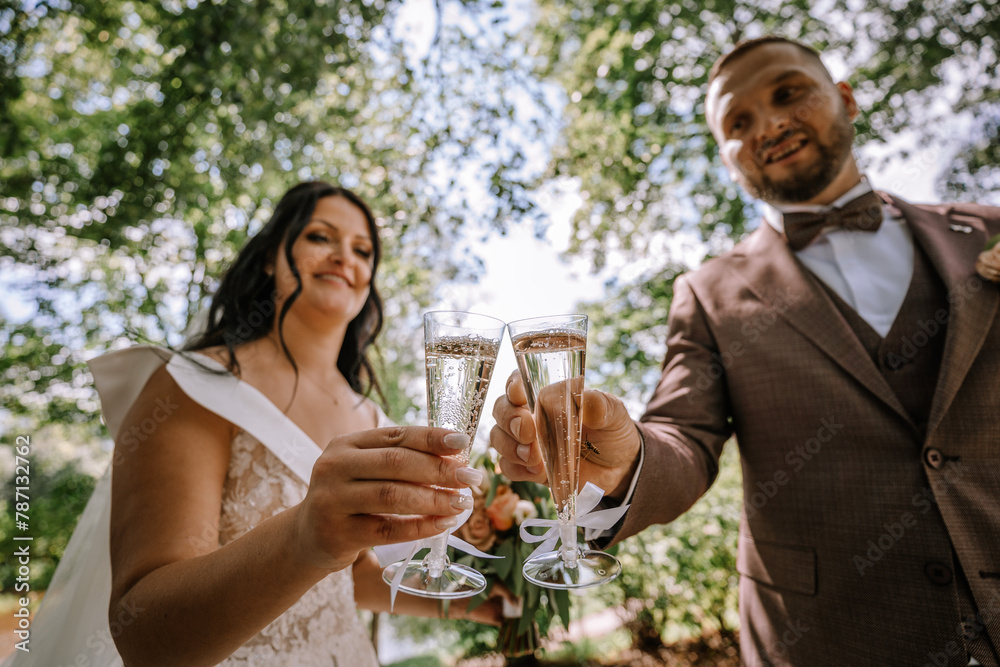 Valmiera, Latvia- July 28, 2024 - A bride and groom are toasting with champagne glasses, smiling on their wedding day in an outdoor setting.