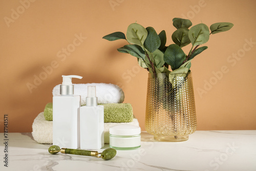 Skin care products in the bathroom. Face cream, serum bottle, jade roller and stack of towels.
