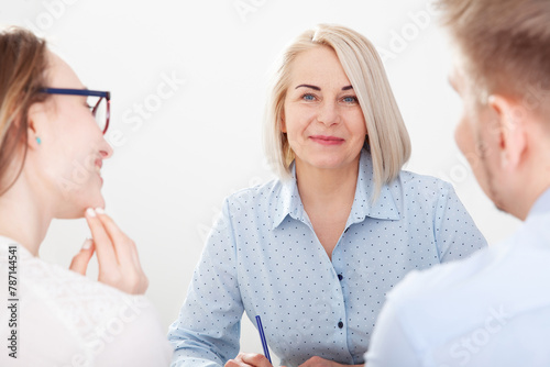 A well-versed woman realtor advises a young couple about real estate in the office.