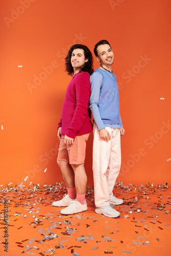 merry good looking gay friends in stylish clothes with makeup posing under confetti rain, pride photo