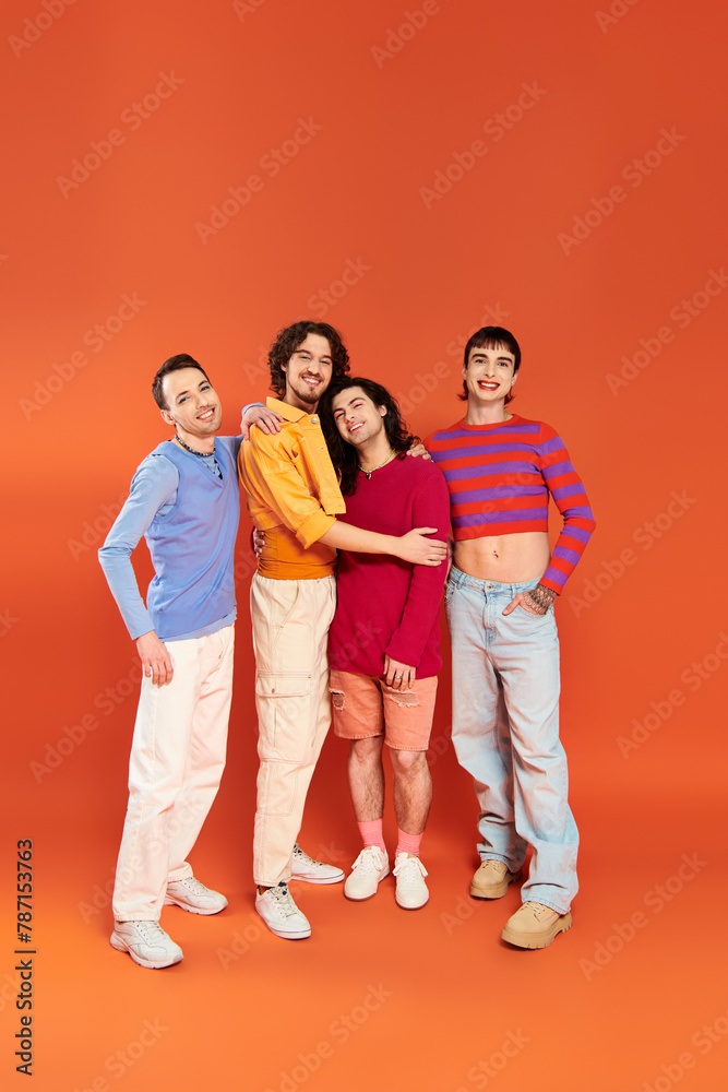 Fototapeta premium four handsome cheerful gay men in vibrant clothes posing together on orange backdrop, pride month