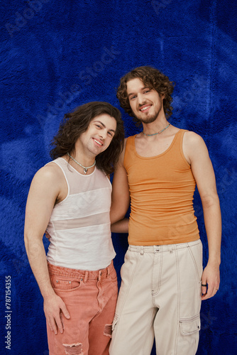 cheerful attractive elegant gay friends in cozy outfits on dark blue backdrop, pride month photo