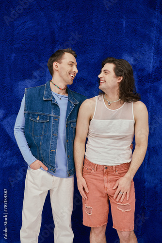 positive attractive elegant gay friends in cozy outfits on dark blue backdrop, pride month