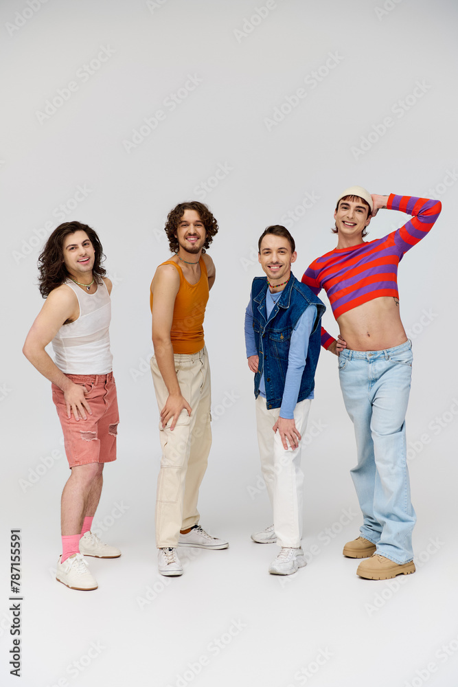 Fototapeta premium four joyous good looking gay men in vivid attires smiling at camera while posing on gray backdrop
