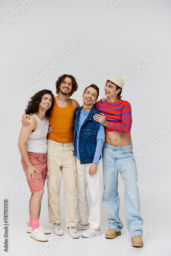 four merry good looking gay men in vivid attires smiling at camera while posing on gray backdrop photo