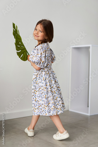 A young girl in summer clothes is smiling, holding a palm leaf with an outstretched hand