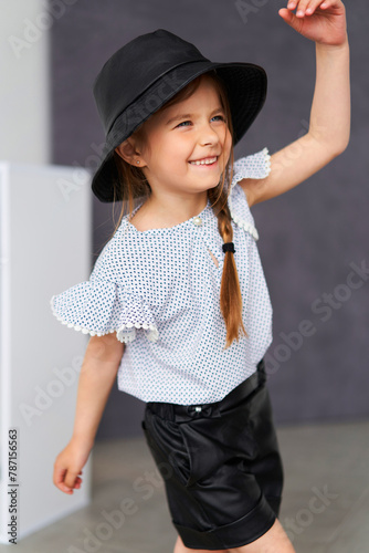 A little girl in a dress and matching hat, posing in the sun and smiling brightly