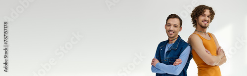 joyful lgbtq friends in stylish outfits posing on gray backdrop and looking at camera, banner photo