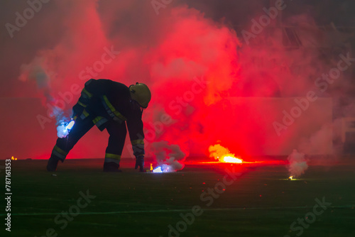 Fireman picking up burning torches during a football match.  Football fans' torches fire on the field photo