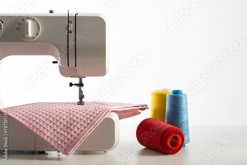 Part of a white sewing machine with a piece of pink fabric and skeins of thread on a white background, close-up. White background. Tailoring services, copy space for text, modern photo