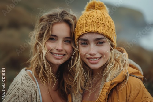 Two smiling young women, one donning a yellow beanie, enjoy an autumnal day outdoors with soft focus background of nature