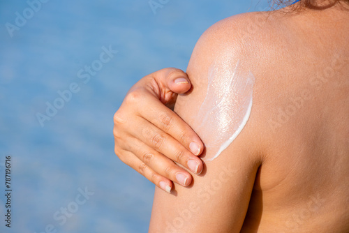 A woman is applying sunscreen and skin care to protect her skin from UV rays. She is applying sunscreen on her hands and arms. The sun symbol is a very sunny background. Health and skin care concept	