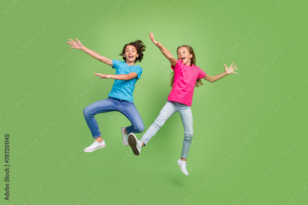Full length photo of funky positive friends wear t-shirts jumping high having fun isolated green color background Full length photo of funky positive friends wear t-shirts jumping high having fun isolated green color background