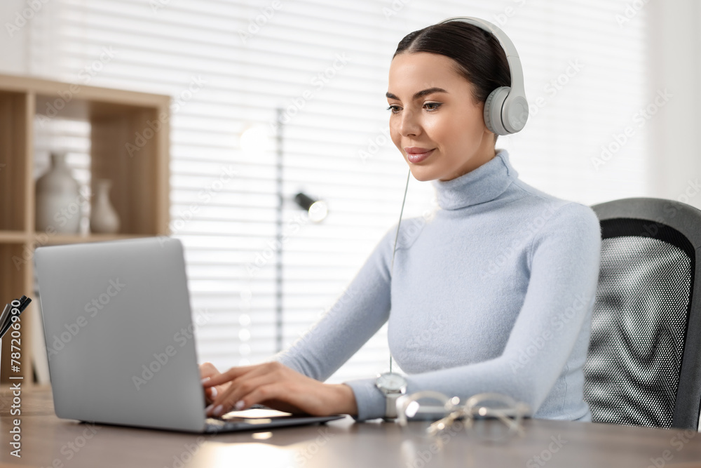 Young woman in headphones watching webinar at table in office Young woman in headphones watching webinar at table in office