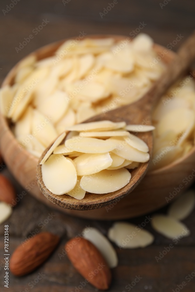Fresh almond flakes in bowl, spoon and nuts on wooden table, closeup Fresh almond flakes in bowl, spoon and nuts on wooden table, closeup