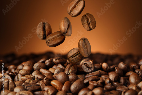Roasted coffee beans falling on heap against brown background, closeup