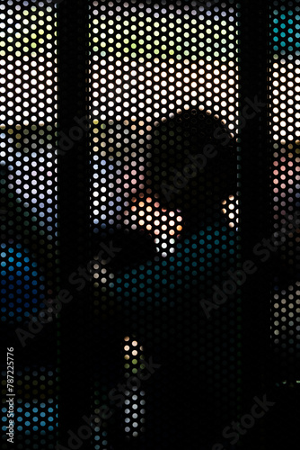 Holes.  The silhouette of a woman is seen through holes in a mesh fence in a market in Bangkok.