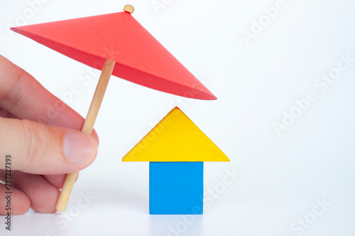 House shape toy covered with red umbrella representing house or property insurance concept