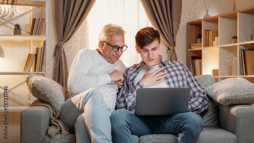 Internet leisure. Family generation. Online research. Happy inspired father and son surfing on laptop together home room interior.