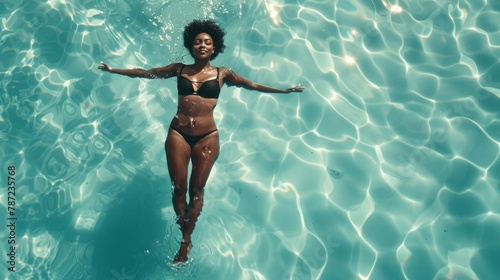Black woman in elegant swimsuit swimming in crystal-clear pool from overhead perspective photo