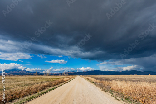 Dark storm clouds over dirt road crossing field photo
