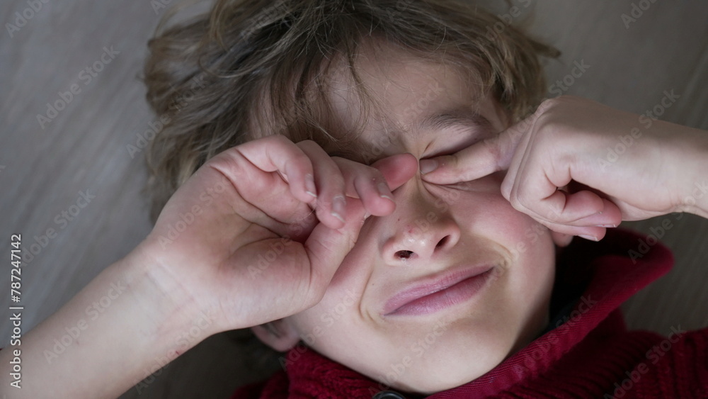 Tired young boy rubbing eyes with hands, close-up face of tired kid touching face with itchy eye Tired young boy rubbing eyes with hands, close-up face of tired kid touching face with itchy eye
