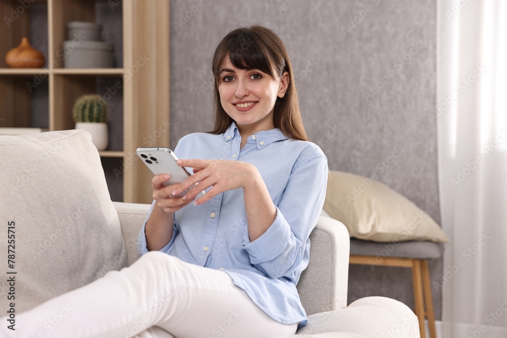 Beautiful young housewife using smartphone on sofa at home Beautiful young housewife using smartphone on sofa at home