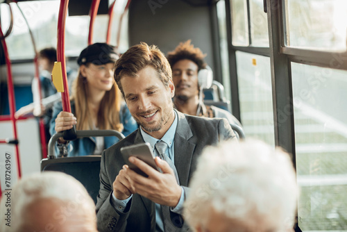 Smiling young adult businessman using smartphone on the bus photo