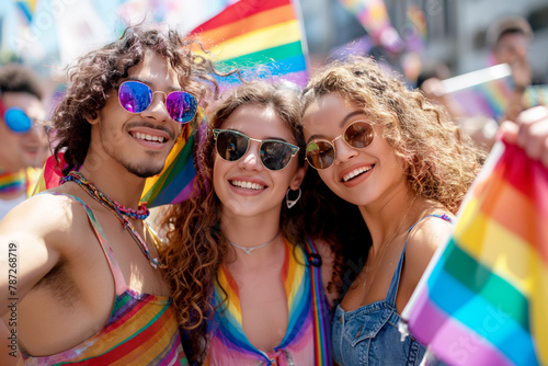 pride festival, two happy young people with curly hair and sunglasses holding a rainbow flag smiling at the camera