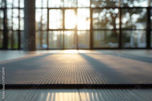 Grey fitness mat on a floor in a blurred yoga studio on background.