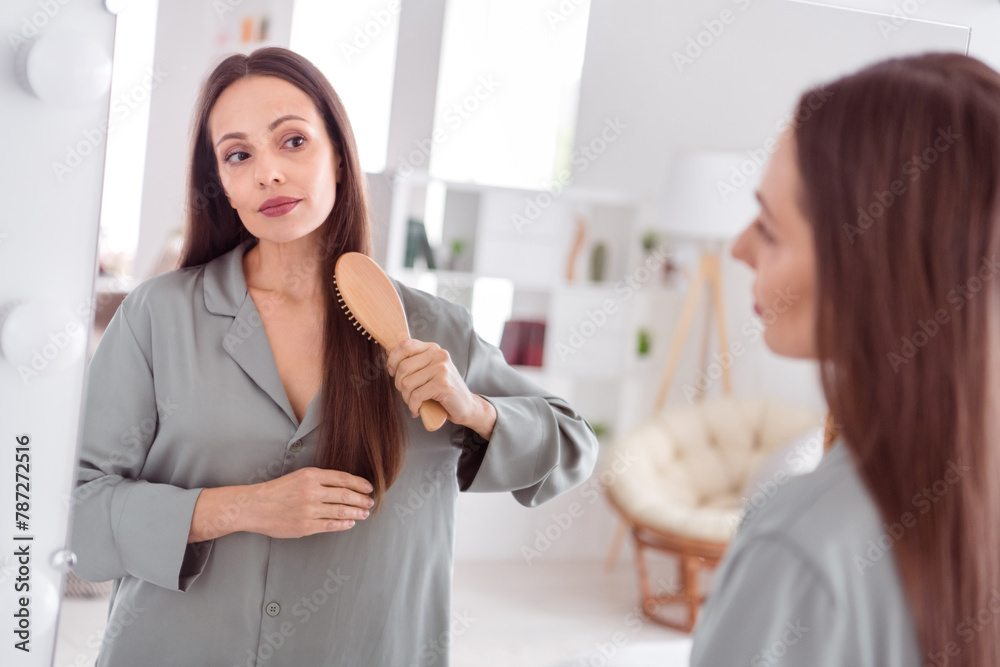 Photo of adorable pretty lady wear grey nightwear look mirror brushing hair indoors apartment bedroom