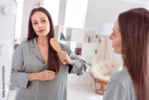 Photo of adorable pretty lady wear grey nightwear look mirror brushing hair indoors apartment bedroom